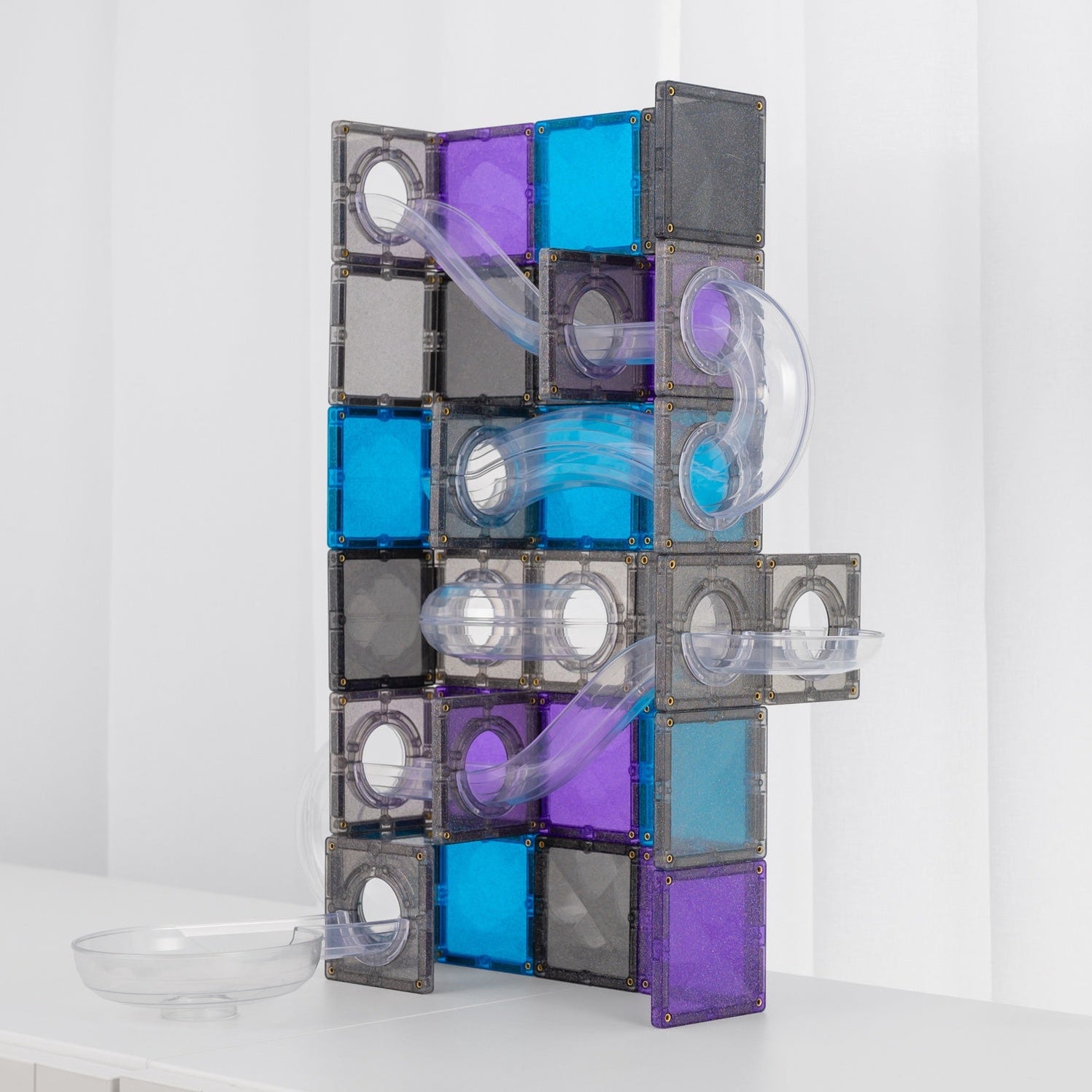 A modular magnetic tile play structure made of translucent grey, purple, and blue square tiles with clear curved tubes, standing on a white surface against a white curtain background Connetix new Galaxy Pack Spotty Dot Toys
